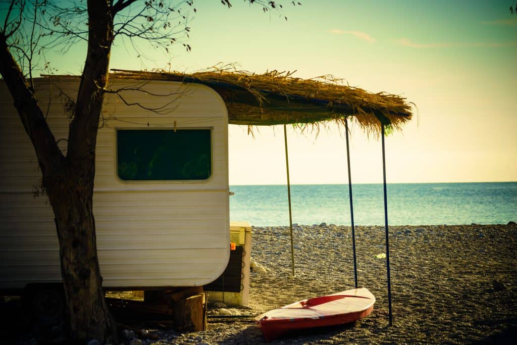 Travel trailer on the beach with grass awning cover.